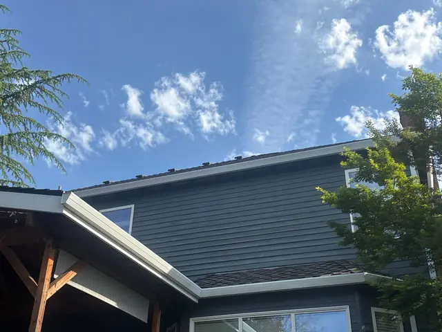 White gutters following the upper and lower roof edges of a two-story gray home in Beaverton