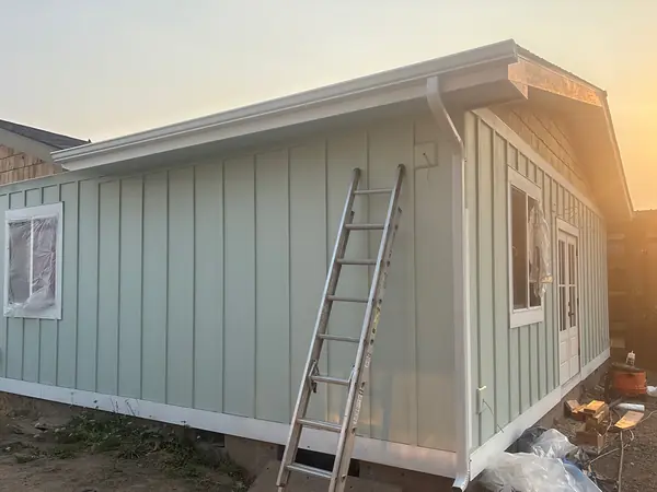 New sage-green board-and-batten addition in Hillsboro with a new white seamless gutter and downspout