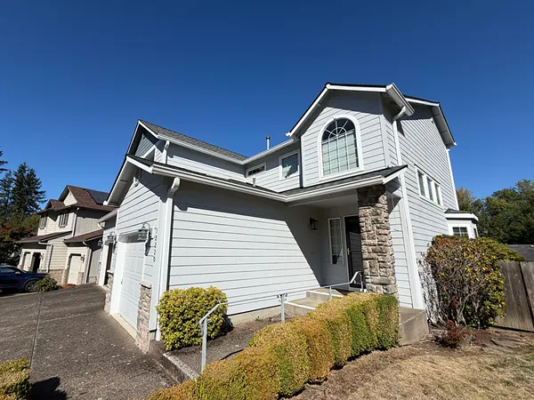 Two-story light gray home with white seamless gutters along multiple rooflines and a stone-trimmed entry