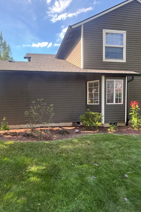 Dark brown two-story home with matching black gutters and downspouts above a green lawn