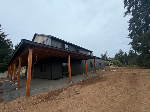 Dark new-construction home with a long timber-post porch and black gutters on freshly graded ground