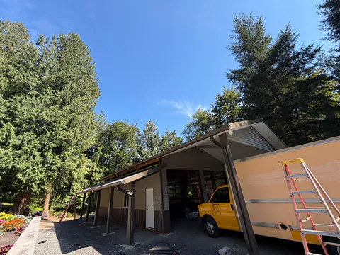 Two-tone shop with a lean-to on dark posts, bronze gutters and downspouts and a parked box truck