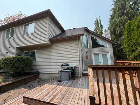 Back of a tan two-story home with brown gutters on several rooflines above a wood deck