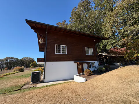 Brown wood chalet-style home with a white lower story and dark gutters under wide eaves