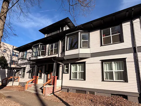 Large white multi-unit craftsman building with dark trim and dark gutters and downspouts