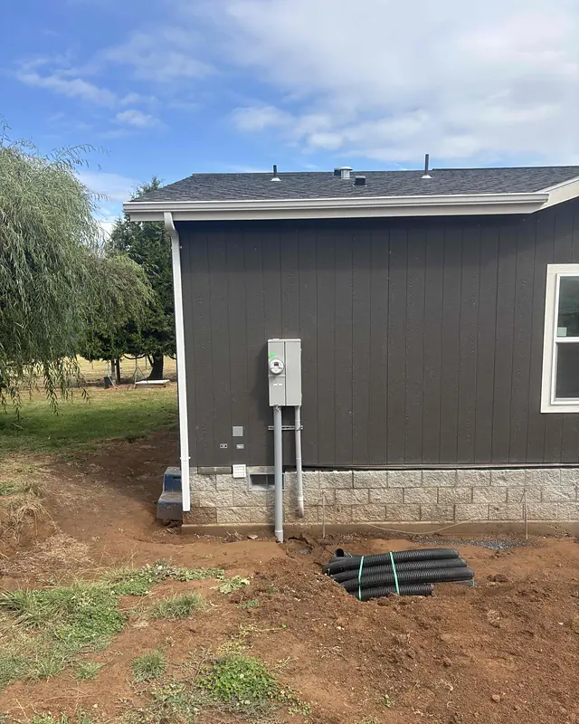 White downspout running down the corner of a dark-sided Deer Island home from a new seamless gutter, with a weeping willow beside it
