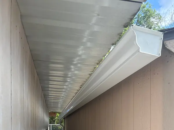 View up at a new white gutter with an end cap fastened tight along the eave of a Beaverton building, with the soffit beside it