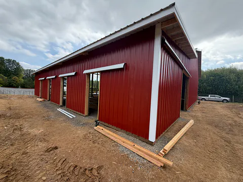 New red metal pole barn with white trim and a gutter along the eave on freshly graded ground