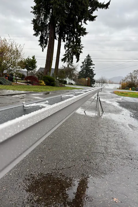 Long white seamless gutter run laid out on a residential street on a rainy day
