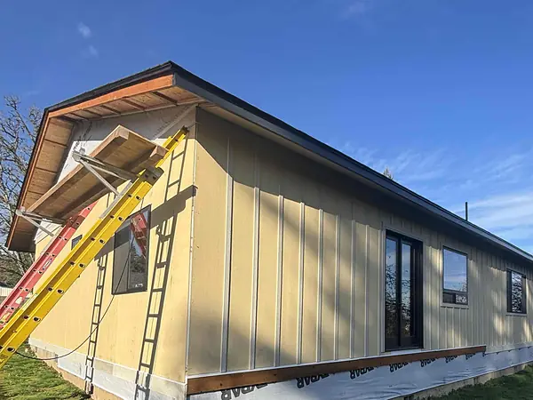 Bare new wood along the roof edge of a Scappoose home being re-sided, with ladders set against the wall