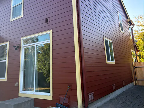 Back of a red two-story home with a color-matched downspout running to the ground by a patio