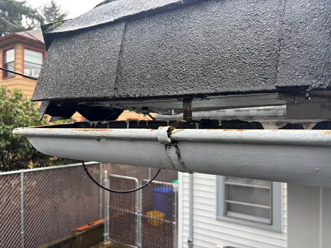 Close-up of an old gutter with a rusted joint separating under the roof edge