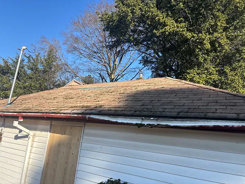 Bent, sagging old gutter along the edge of a moss-covered garage roof