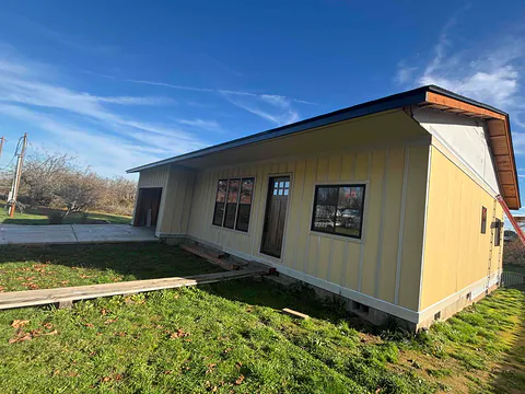 Yellow board-and-batten shop building with gutters along a dark roof edge on a grassy lot