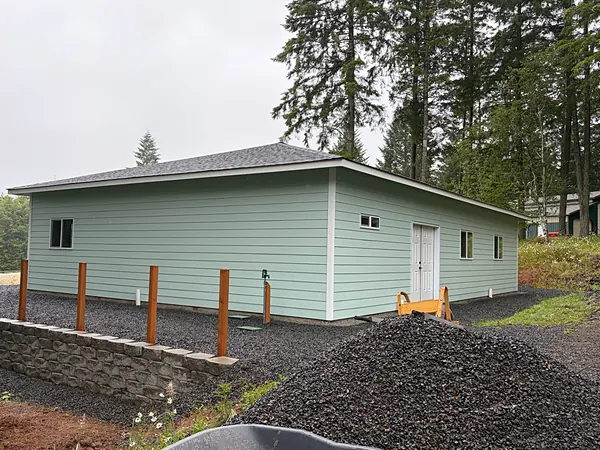 Light green shop building with a hip roof among tall fir trees on a Deer Island, Oregon property