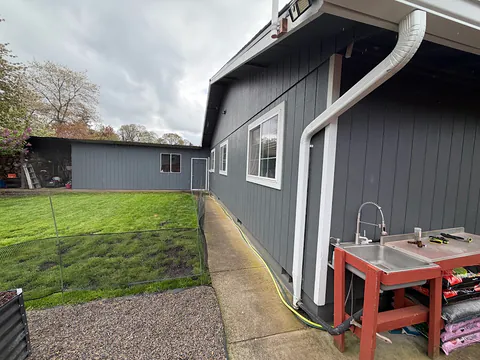 White gutter and downspout running down a dark gray home beside a backyard sink and lawn