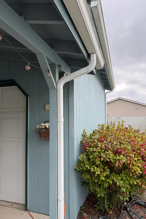 White downspout running down a light blue home beside a covered entry and garage door