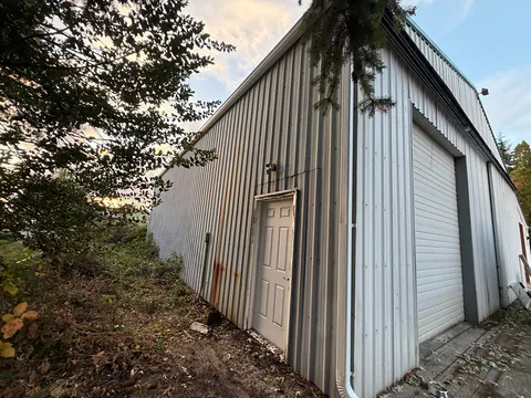 White metal shop building with a roll-up door and a white downspout at the corner