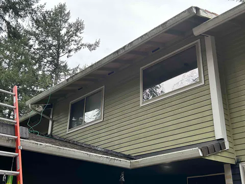 White fascia-style gutters along the upper and lower rooflines of a green two-story home in Oregon City