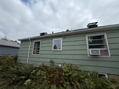 Long side of a sage green shingle-sided home with a white gutter and downspout
