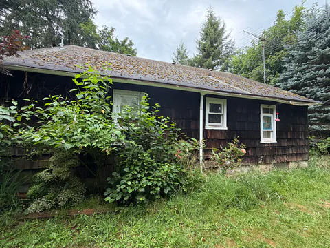 Dark shake-sided ranch home with a moss-covered roof and a white gutter and downspout