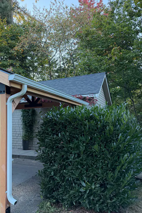 Timber-framed patio cover with a white gutter and a downspout run down the corner post