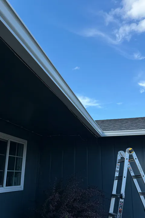 White gutter turning an inside corner on a dark blue home, with an installer's ladder below