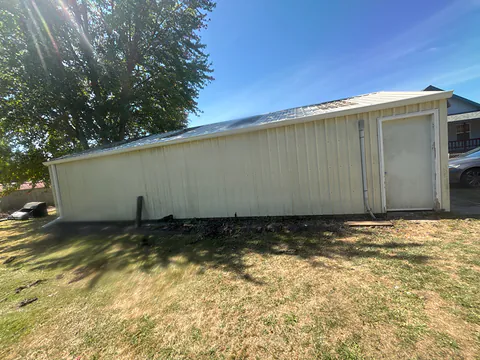 Cream metal shop building with a white gutter and downspout along the eave in Vernonia, Oregon