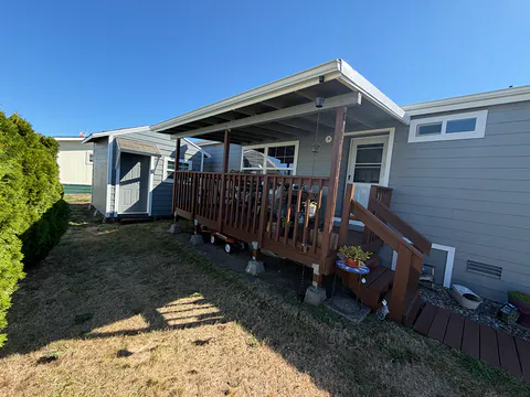 Gray manufactured home with a white patio cover and gutter over a wood deck and stairs