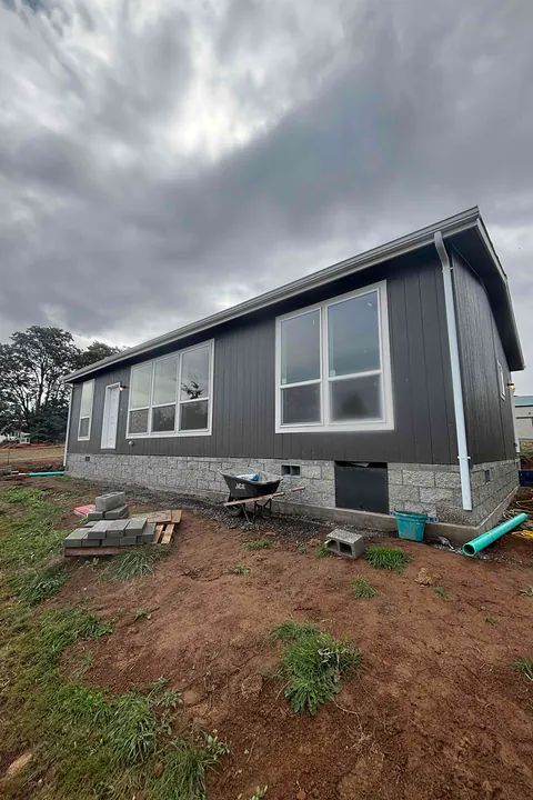 Dark gray manufactured home on a new block foundation with white gutters and a corner downspout