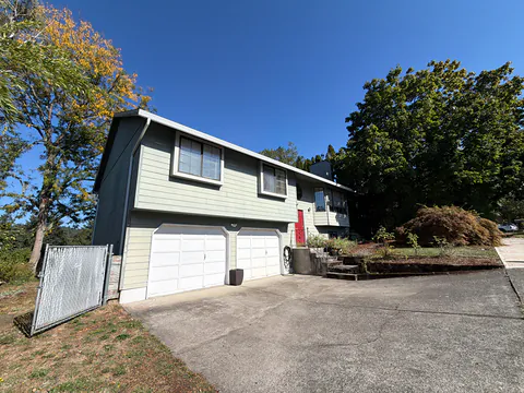 Sage green split-level home with a red front door, a double garage and white gutters