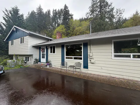 Cream split-level home with navy shutters and white gutters above a wet paved driveway